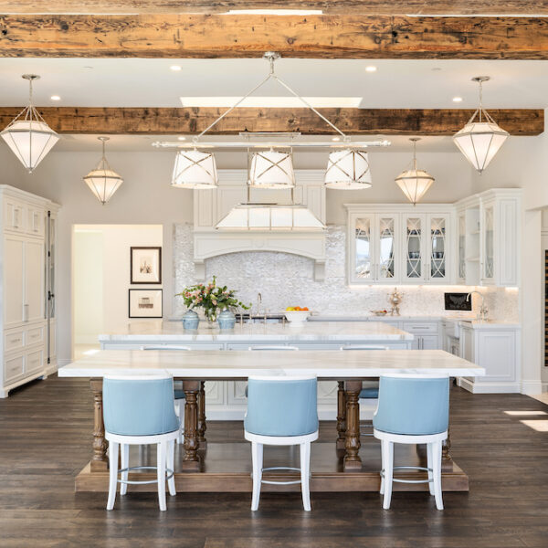 Open white kitchen with blue bar stools and wood beams.
