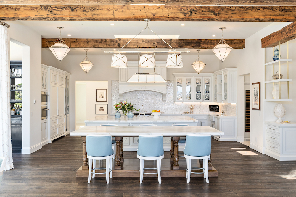 Open white kitchen with blue bar stools and wood beams.