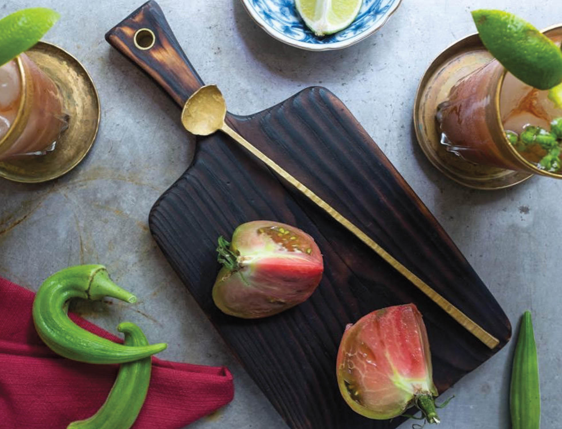 Cut fruit on a dark wood cutting board with a gold stirring spoon and a cocktail glass by Gil Melott