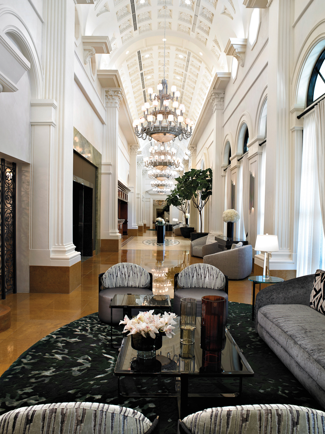 Seating area in a long, white lobby lined with ornate moldings and chandeliers in Acqualina Resort