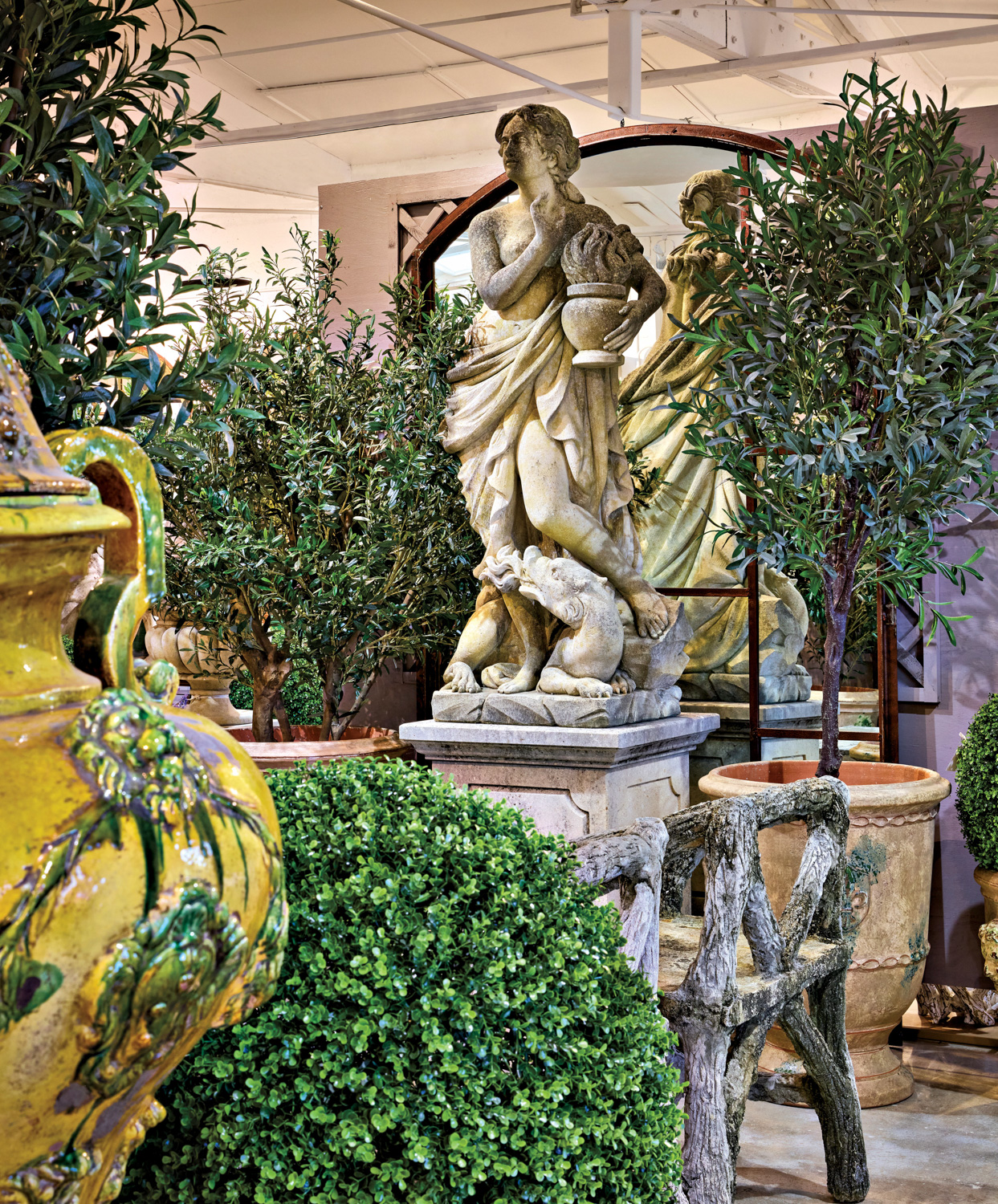 Hand-carved stone statue surrounded by olive trees in vintage pots at the AP Mid Century Modern showroom