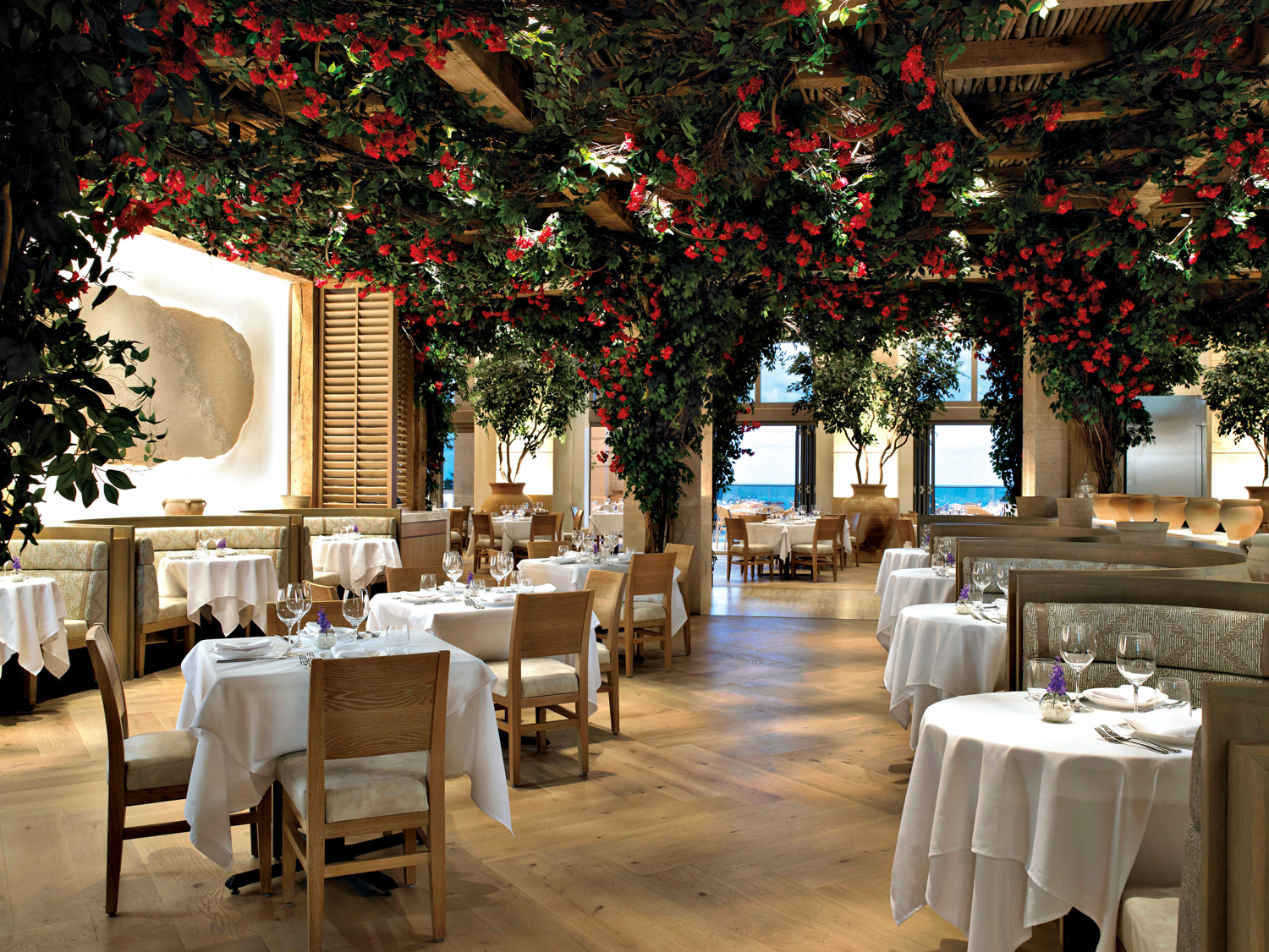 Restaurant with a red flowery ceiling installation and door to outdoor patio seating and water views in Acqualina Resort