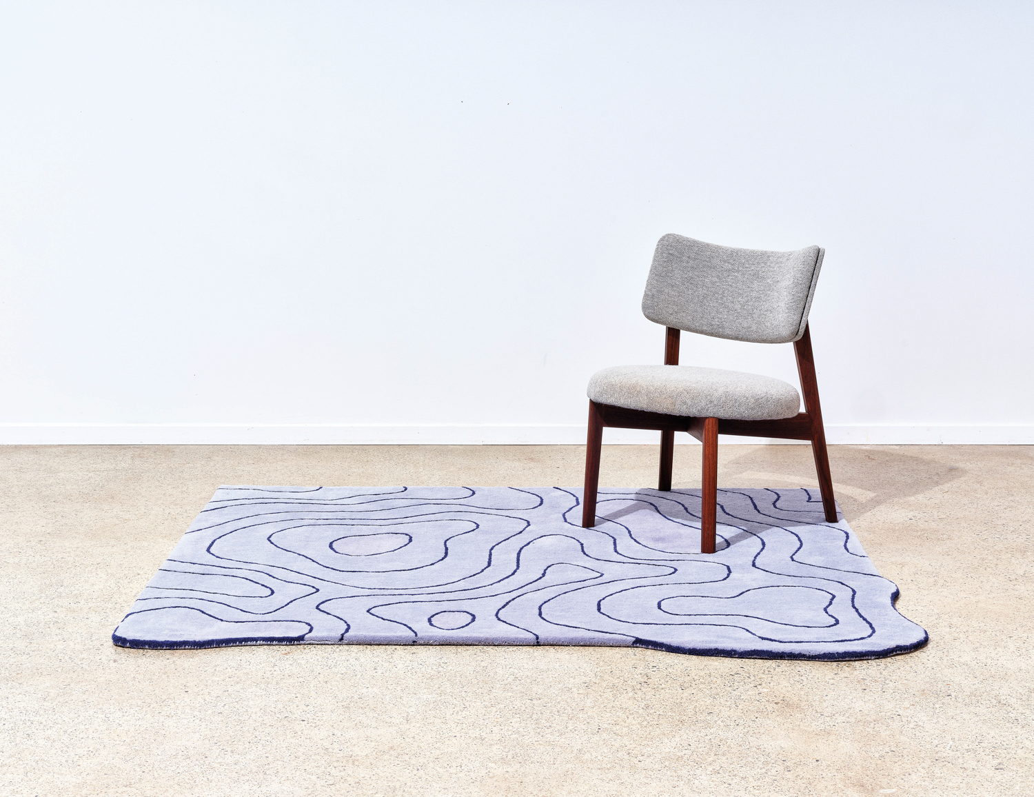 Wood chair with gray upholstered cushions on abstract area rug from Darin Montgomery launch