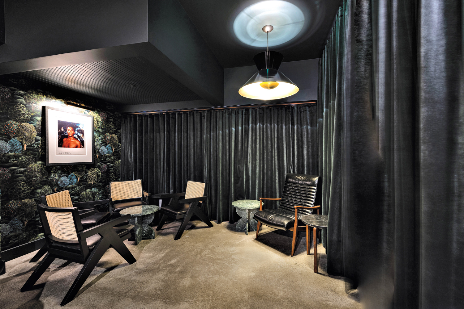 Sitting area of Sousòl with caned chairs and stone accent tables surrounded by dark velvet curtains