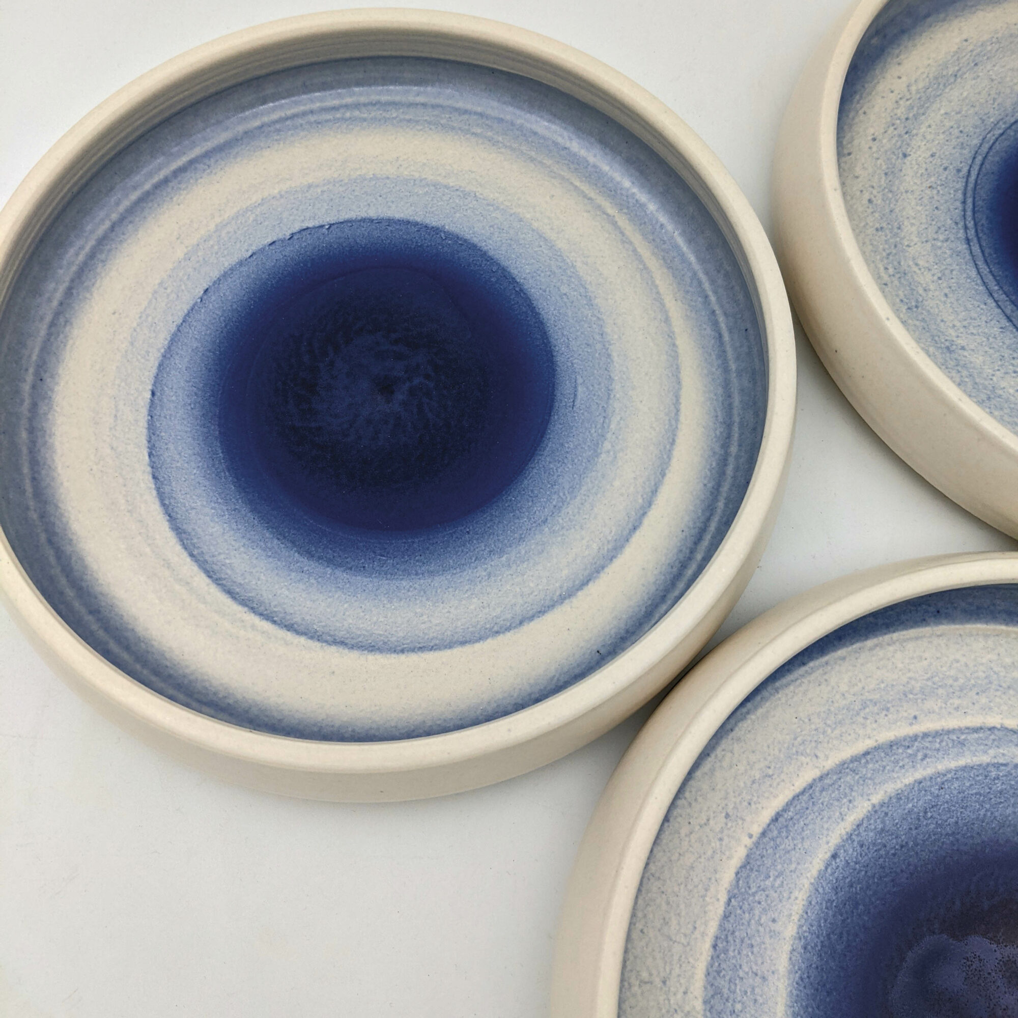 Shallow ceramic bowls featuring a blue ombre design by Jered Nelson