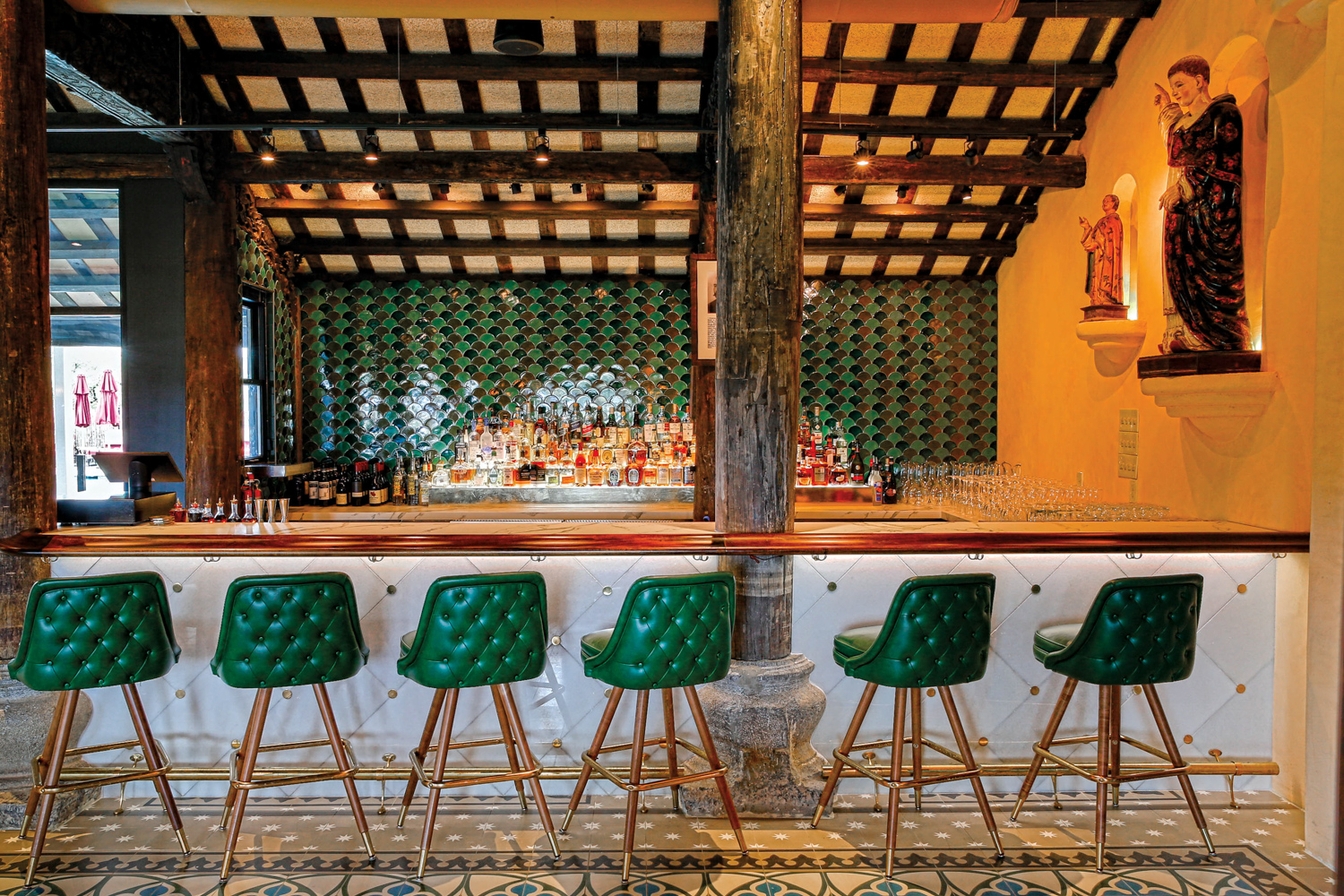 Marble-faced bar with brass buttons with emerald-green bar chairs at Tillie's in Camp Lucy