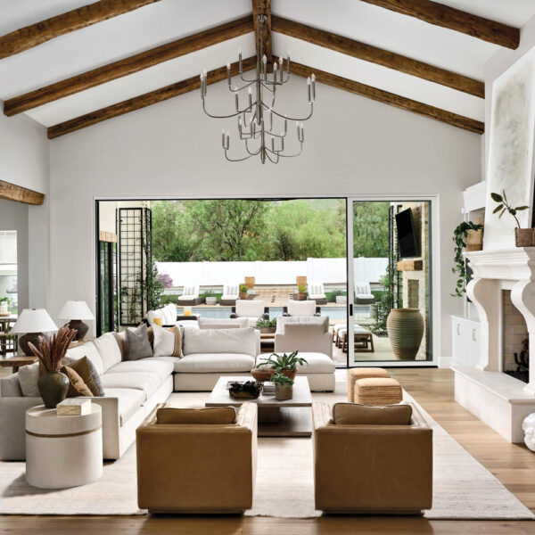 Living room with wood-beam ceilings, white sectionals, tan chairs and limestone fireplace by Lexi Lundberg