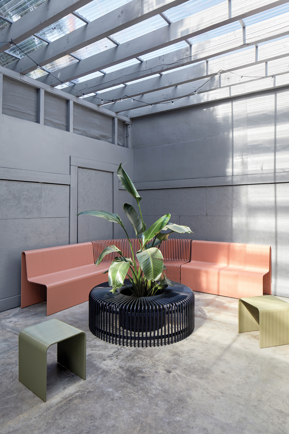 Curved Ribbon outdoor sofa and table by LAUN in a shaded patio with a tall plant in the middle