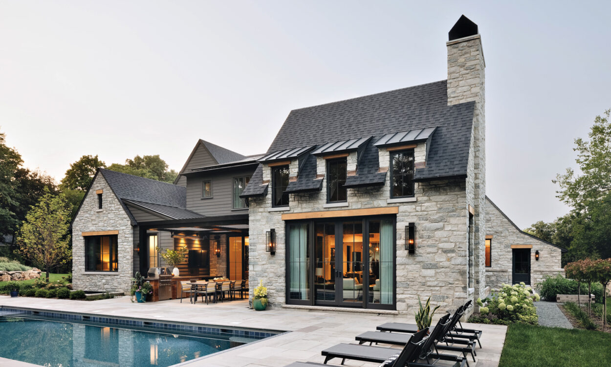 The backyard of a stone home hosts sun loungers and a rectangular pool by Amy Storm