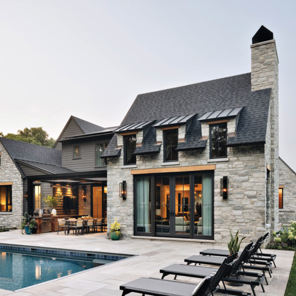 The backyard of a stone home hosts sun loungers and a rectangular pool by Amy Storm