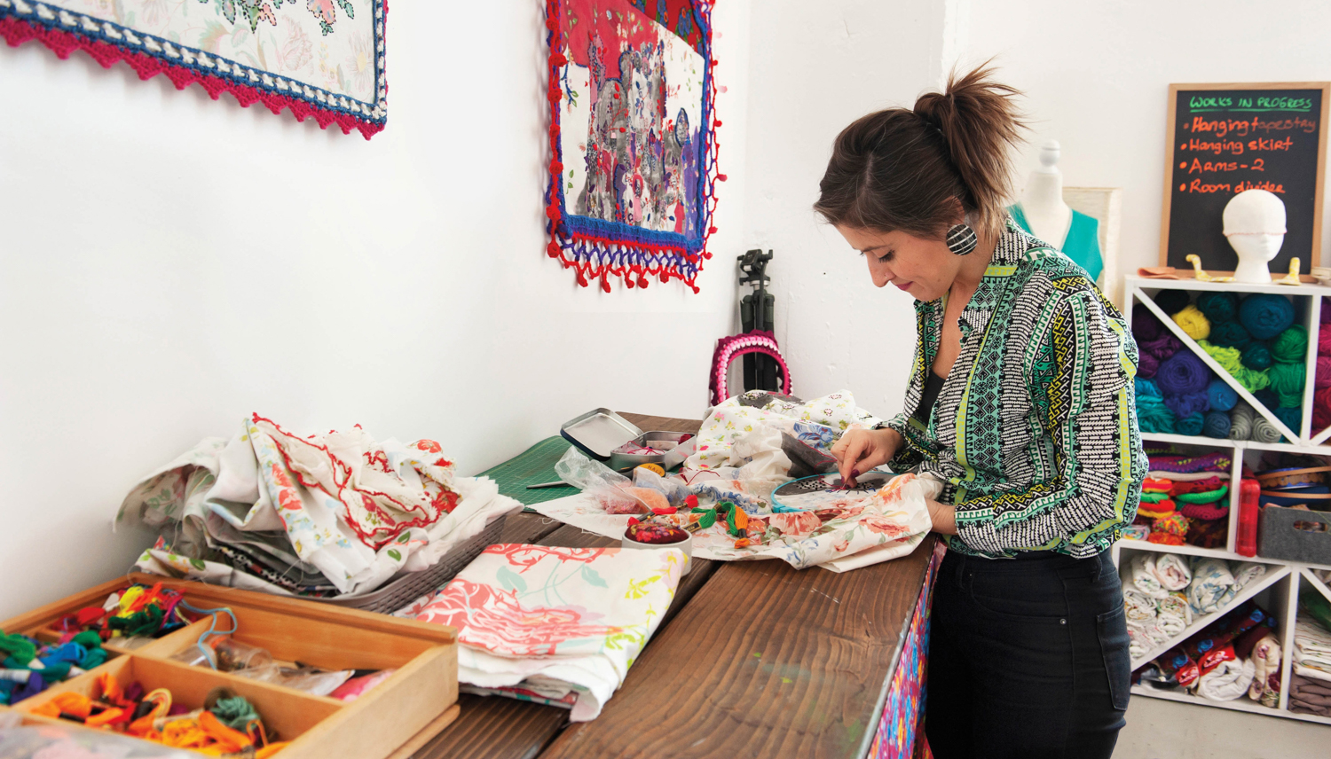 Hale Ekinci embroidering in an art studio filled with yarn and materials