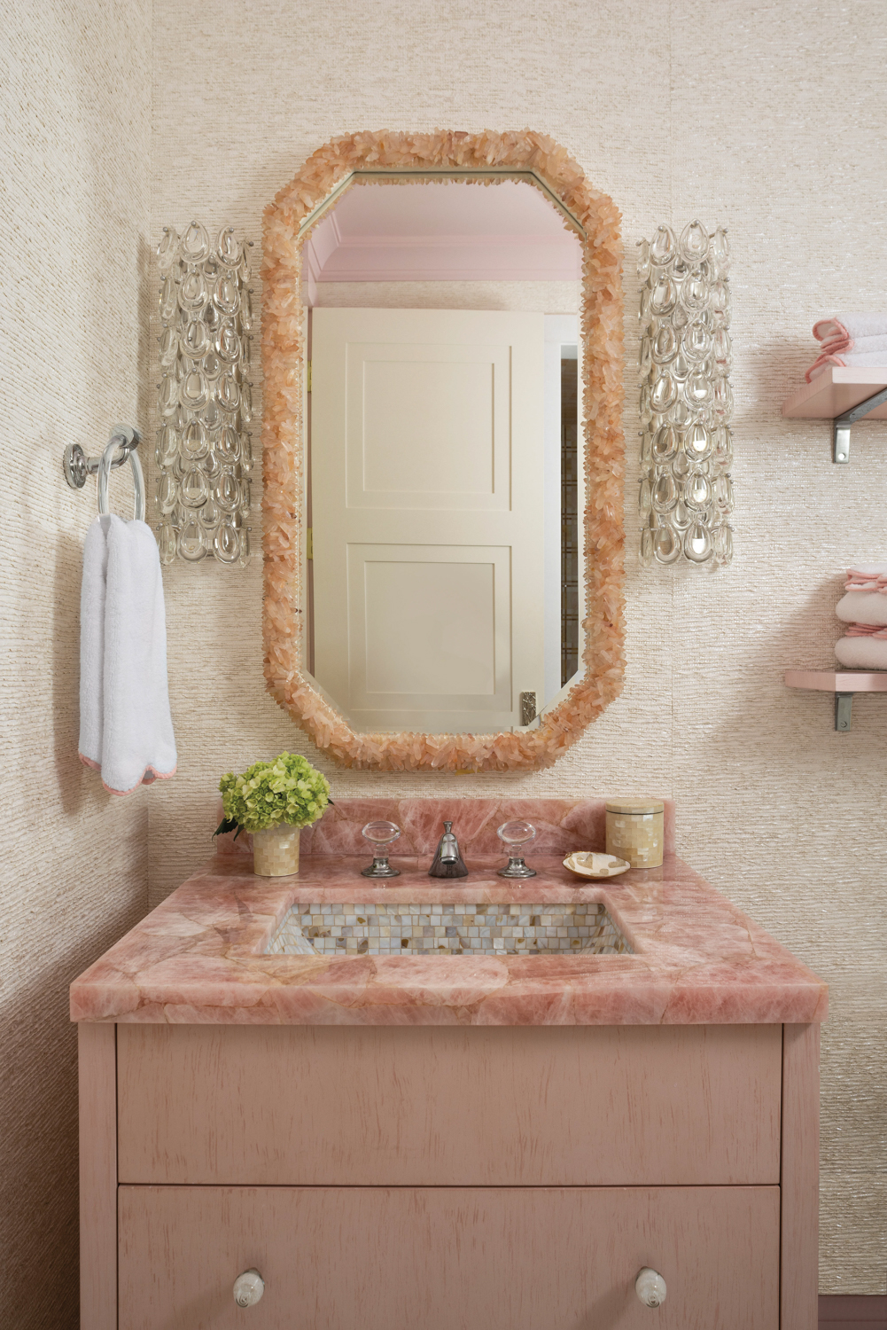 Bathroom vanity with pink countertops, peach mirror and crystal sconces