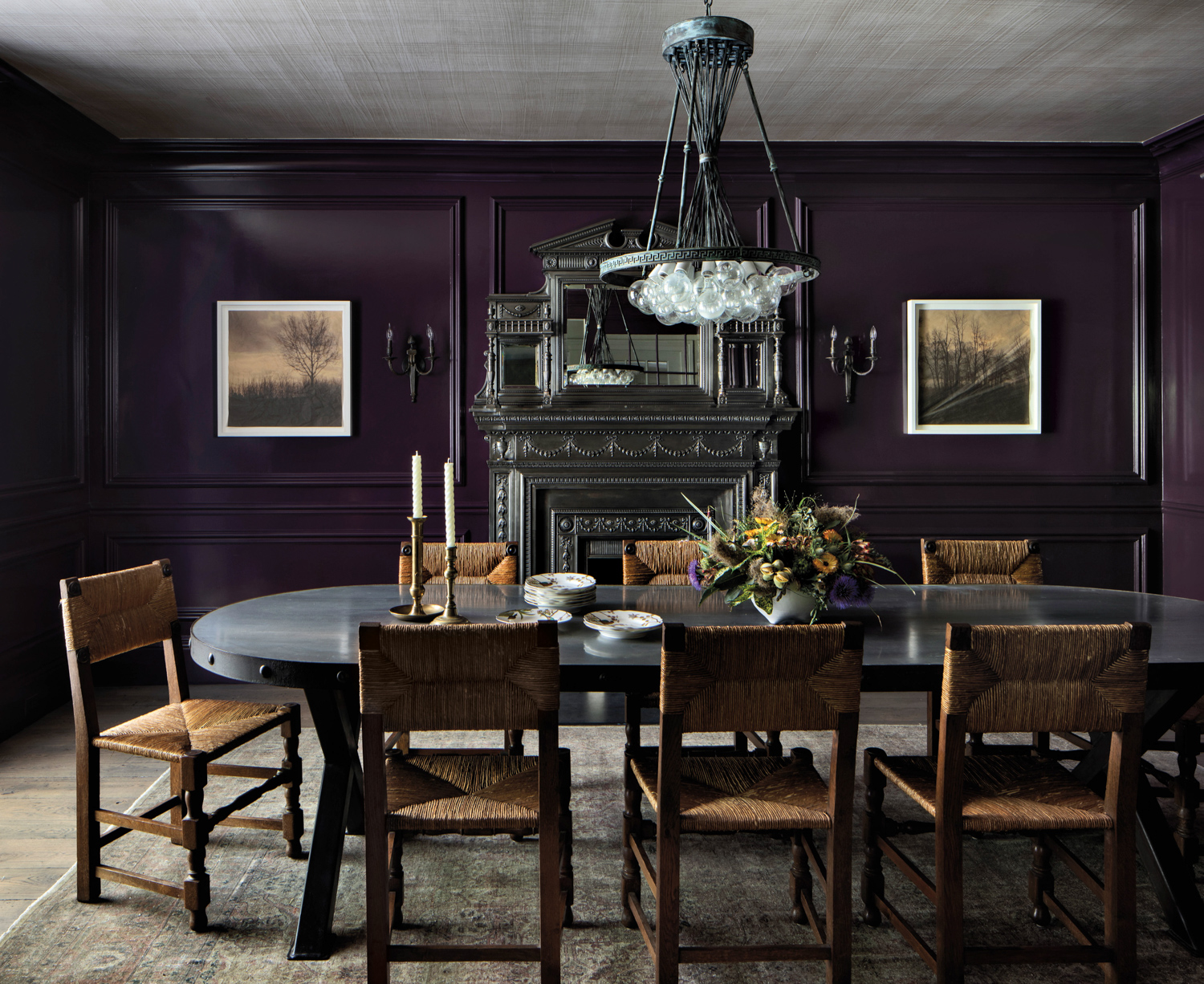 Dining room with dark walls, light fixture, black antique dining table, sepia artwork and French chairs