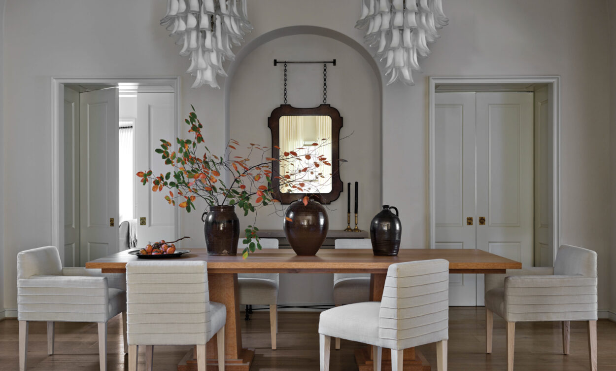 White dining room with wooden table, upholstered chairs and double chandeliers by Anna Booth