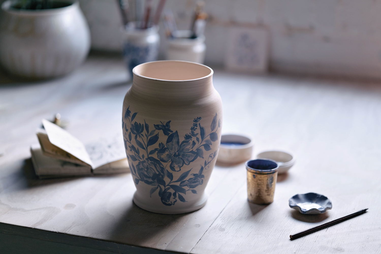 A freshly painted ceramic vessel depicts flowers, leaves and butterflies in an alluring shade of blue