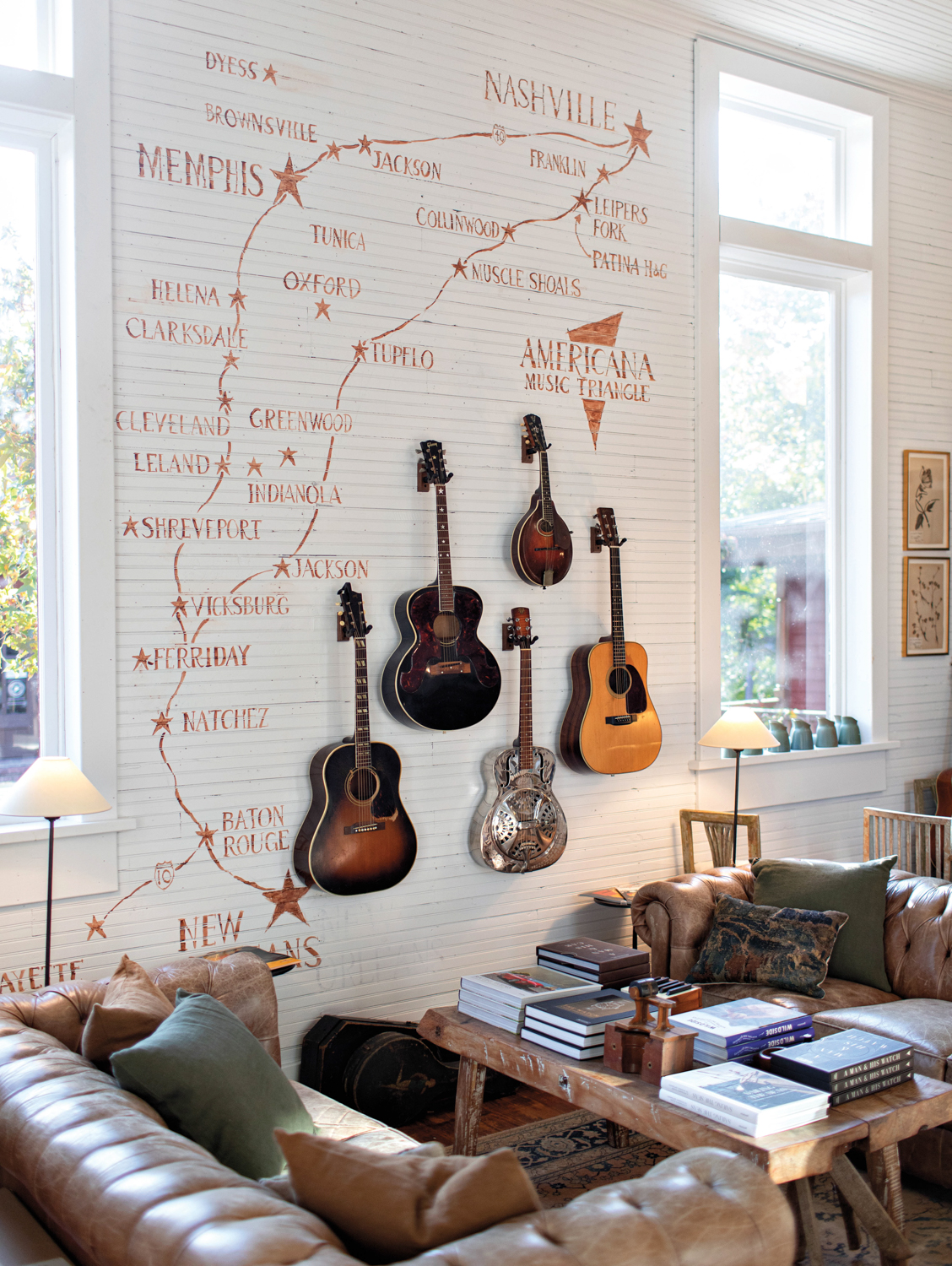 Whitewashed wall with Southeast city names painted on it and 5 guitars hanging in a cluster