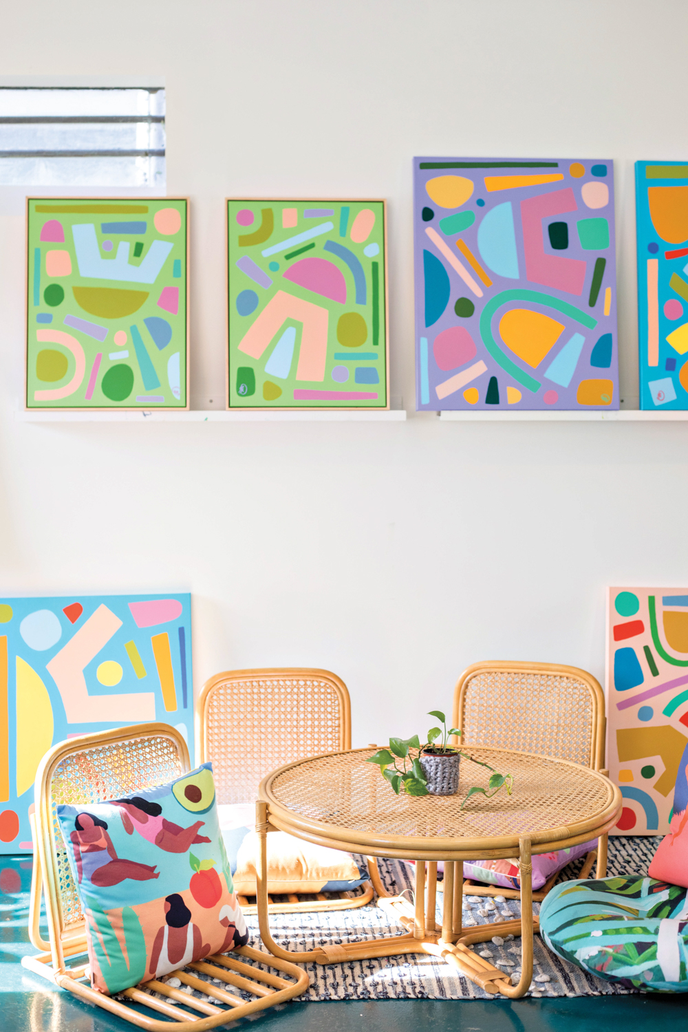 Colorful abstract artwork on ledge shelves and resting on the floor behind low-to-the-ground chairs and table