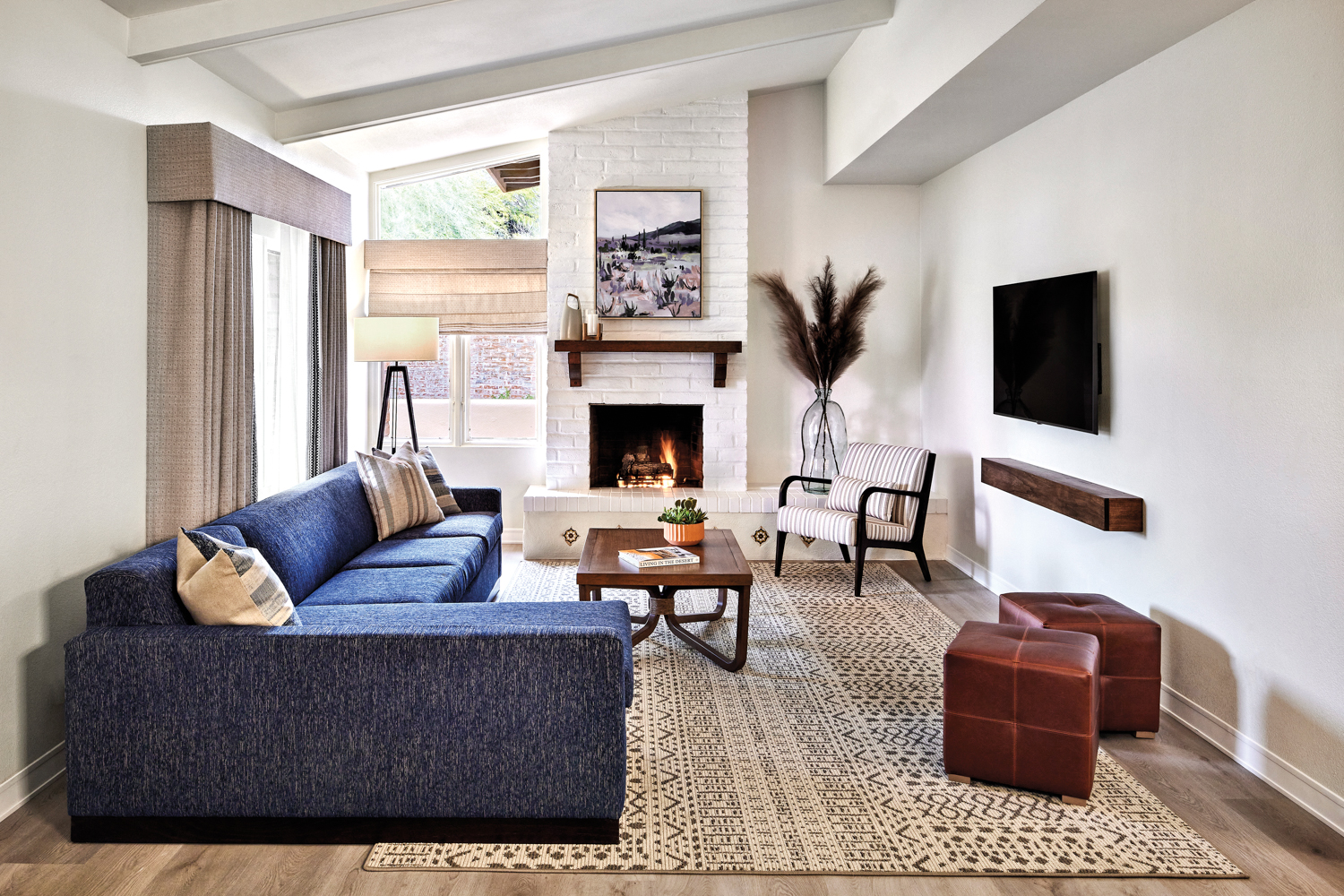 Hotel room with blue sectional atop a neutral patterned rug near a white brick fireplace.