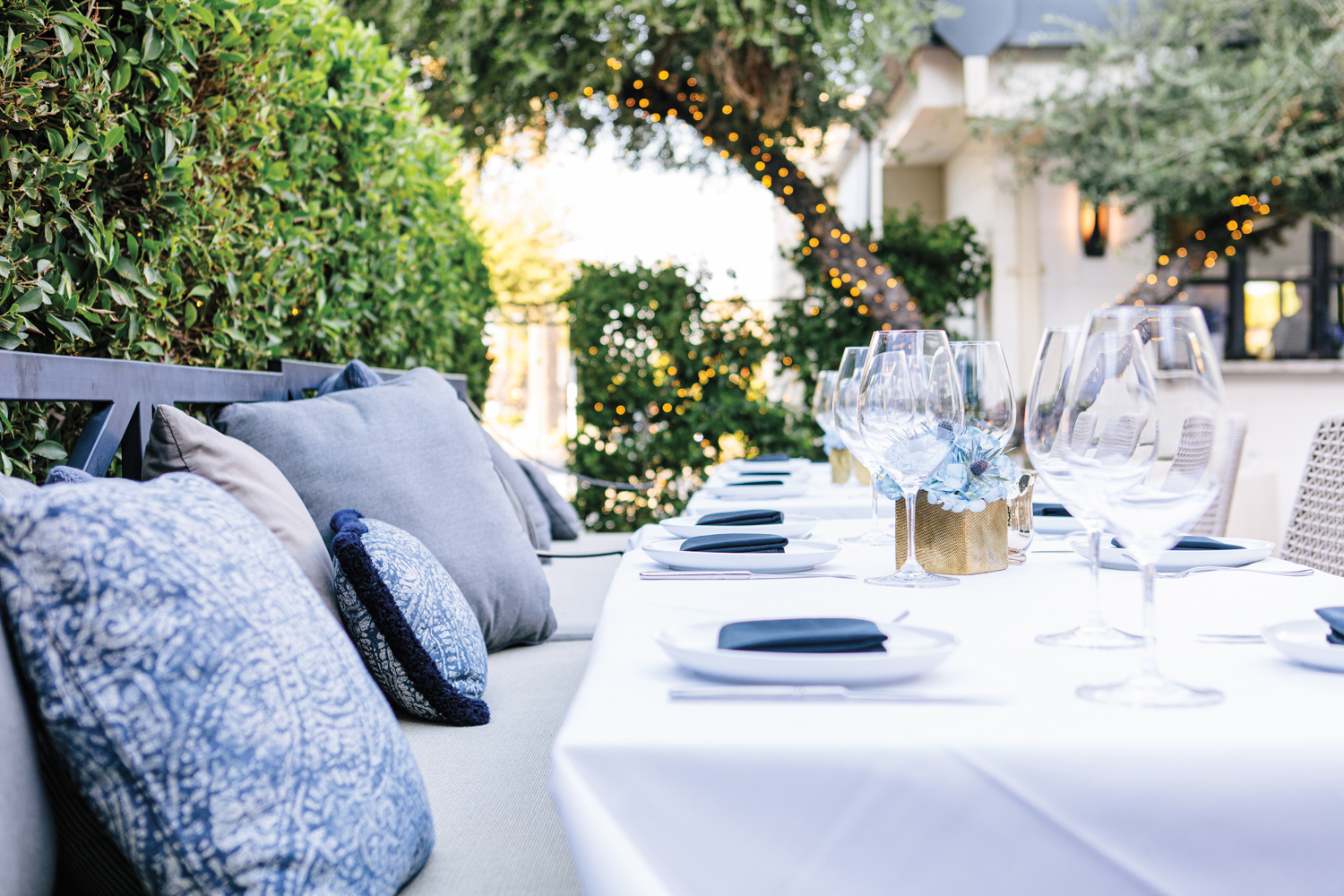 Outdoor dining area with white tablecloths, blue pillows and greenery suggested by Arizona design pros