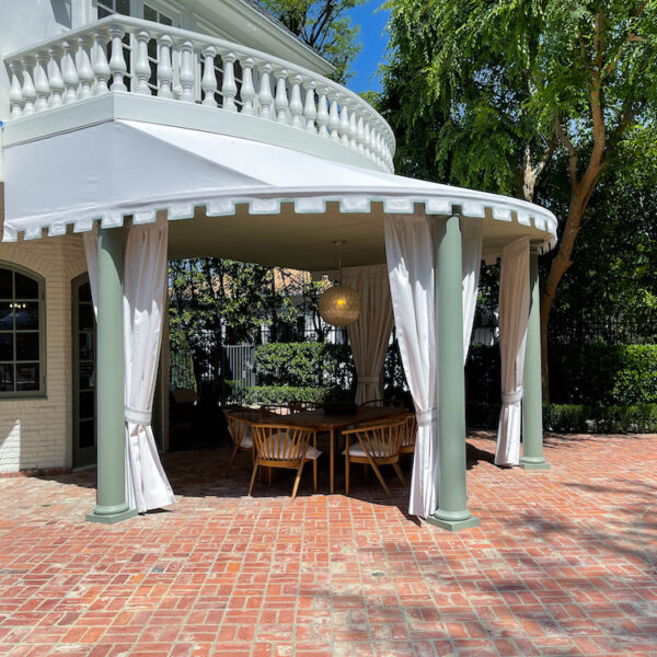exterior of white home with a curved patio with canopy and drapes