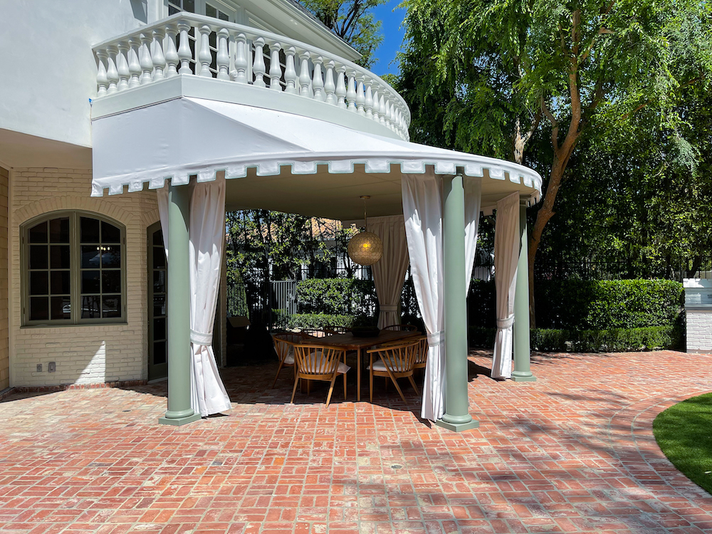 exterior of white home with a curved patio with canopy and drapes