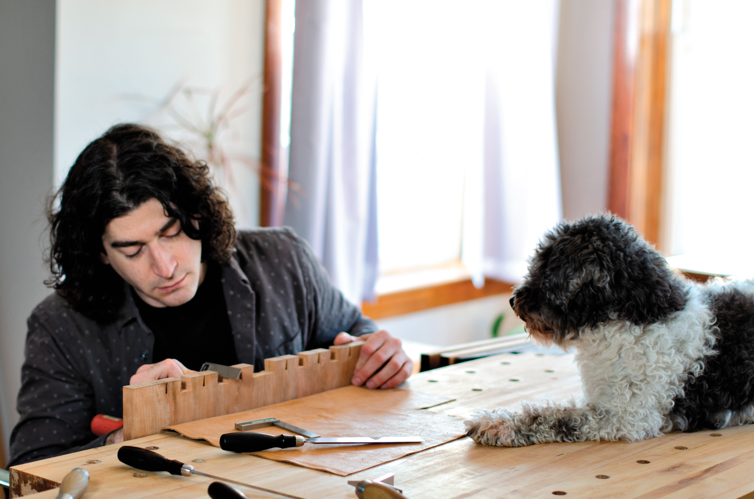 Woodworker Phillip Keefe at work table with black-and-white dog watching him