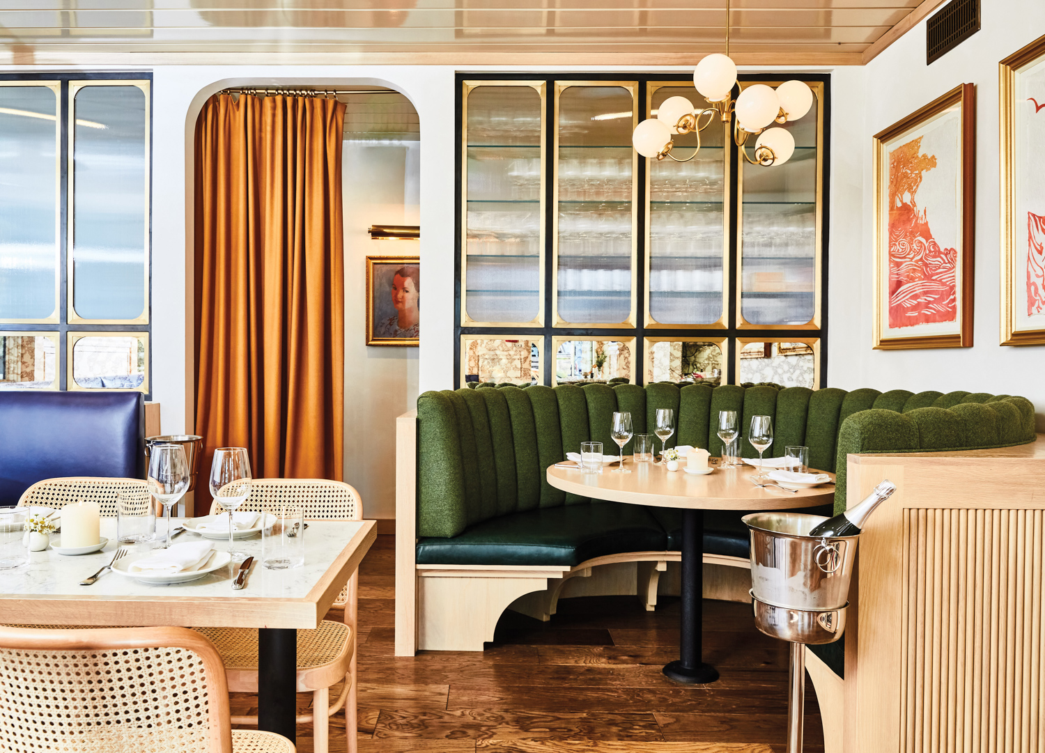 Restaurant with green upholstered circular banquette, gold-framed wall art and wood tables and floors