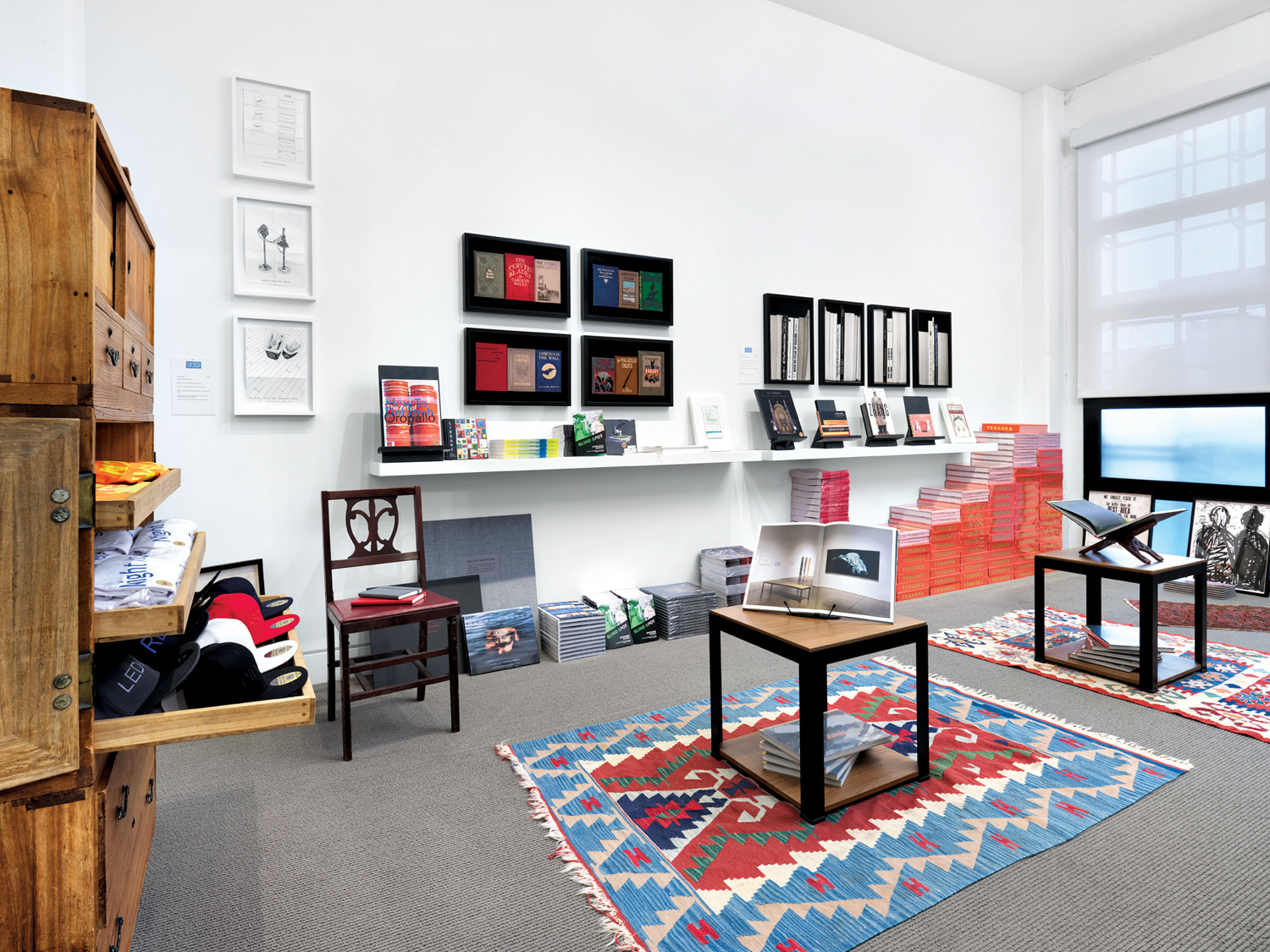 Catharine Clark Gallery store with framed small artworks and tables full of books atop colorful patterned rugs