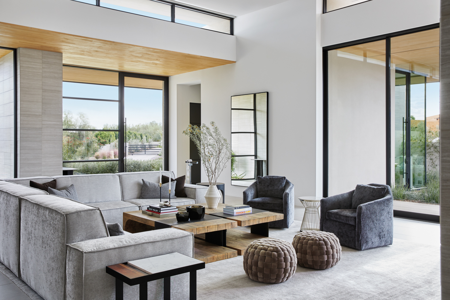 Living room with a light gray sectional, textured ottomans and dark gray swivel chairs by Laura Kehoe