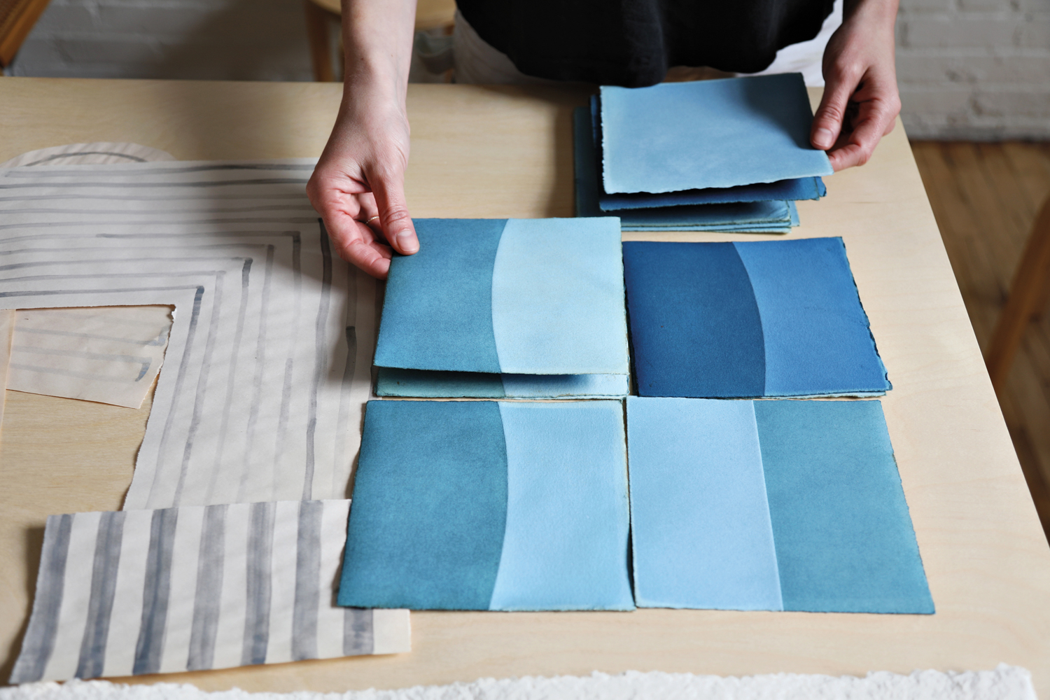 artist holding painted paper samples colored with indigo dye on a desktop workspace