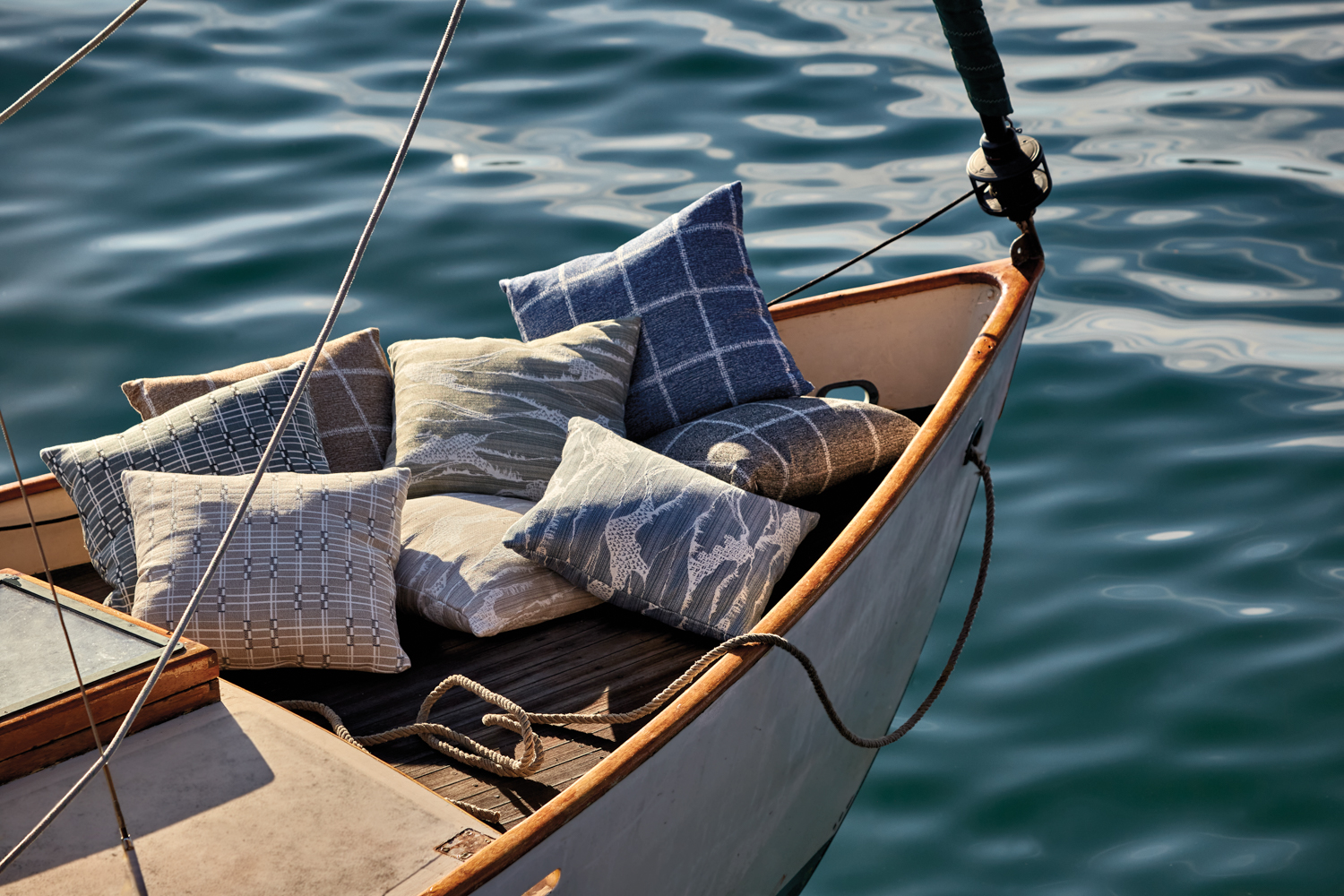 Brook Perdigon pillows covered in blue and gray fabrics strew around the bow of a boat at sea