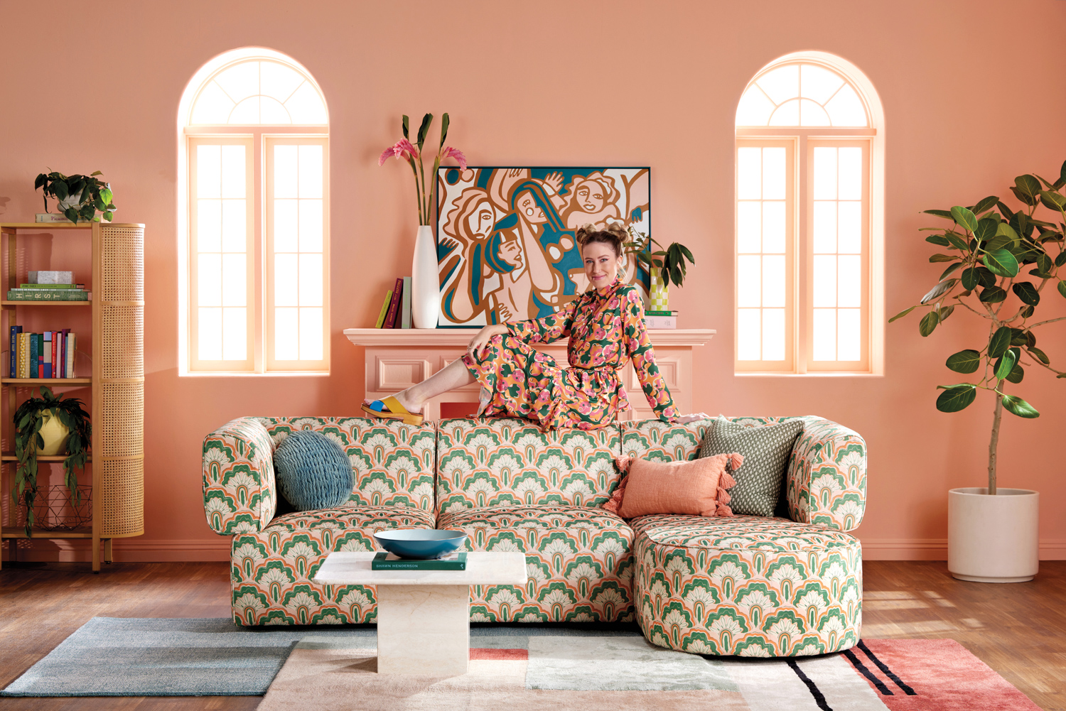 Dani Dazey sitting on a patterned couch in a living room with peach-colored walls and large artwork