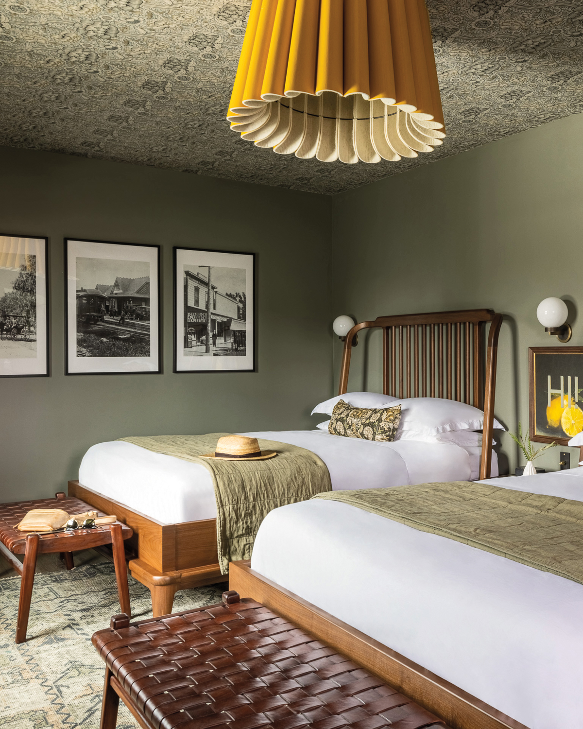 Twin beds in the Richland hotel room with sage-colored walls and a large, pleated yellow pendant light