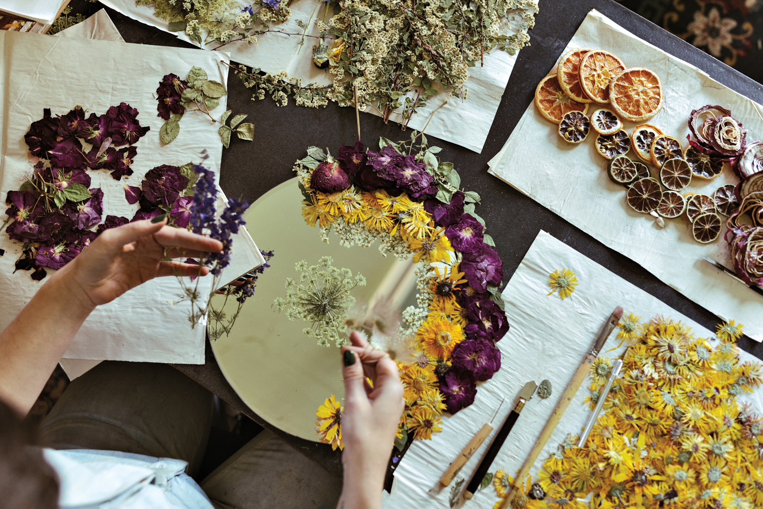 hand placing rows of flowers in rings from the outside in, with flowers on a workspace around the mirror