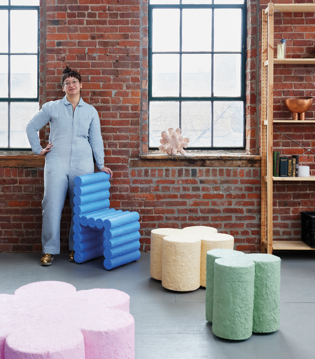 Furniture maker Hannah Bigeleisen leaning against blue chair with brick backdrop
