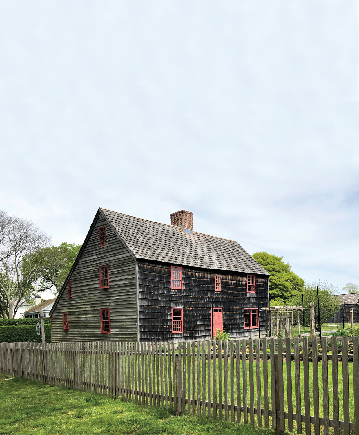 exterior of black wooden farmhouse with red windows, grass and fence