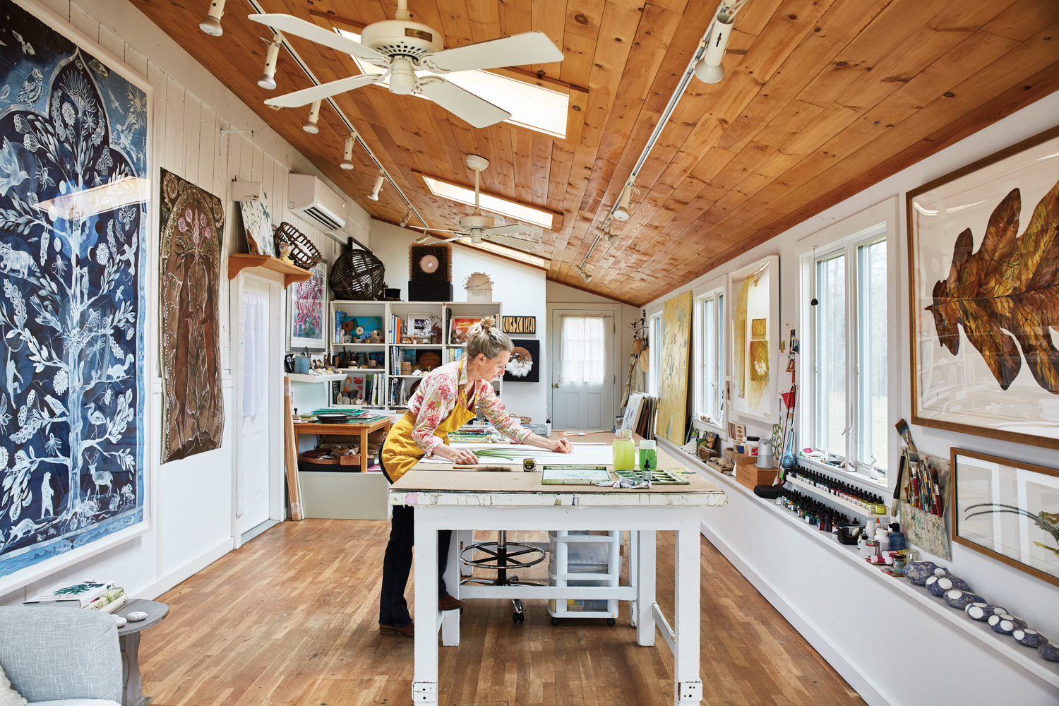 Idoline Duke in her studio over a table with her art hanging behind her