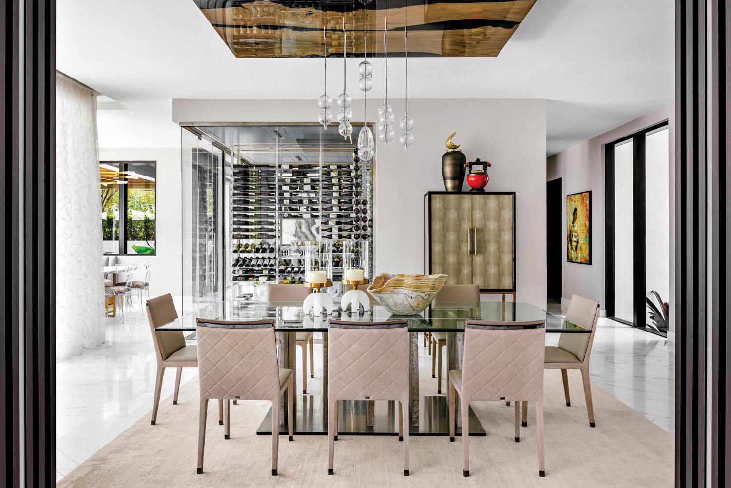 dining area with glass table, cream-colored chairs and glass chandelier in home by Nicole White