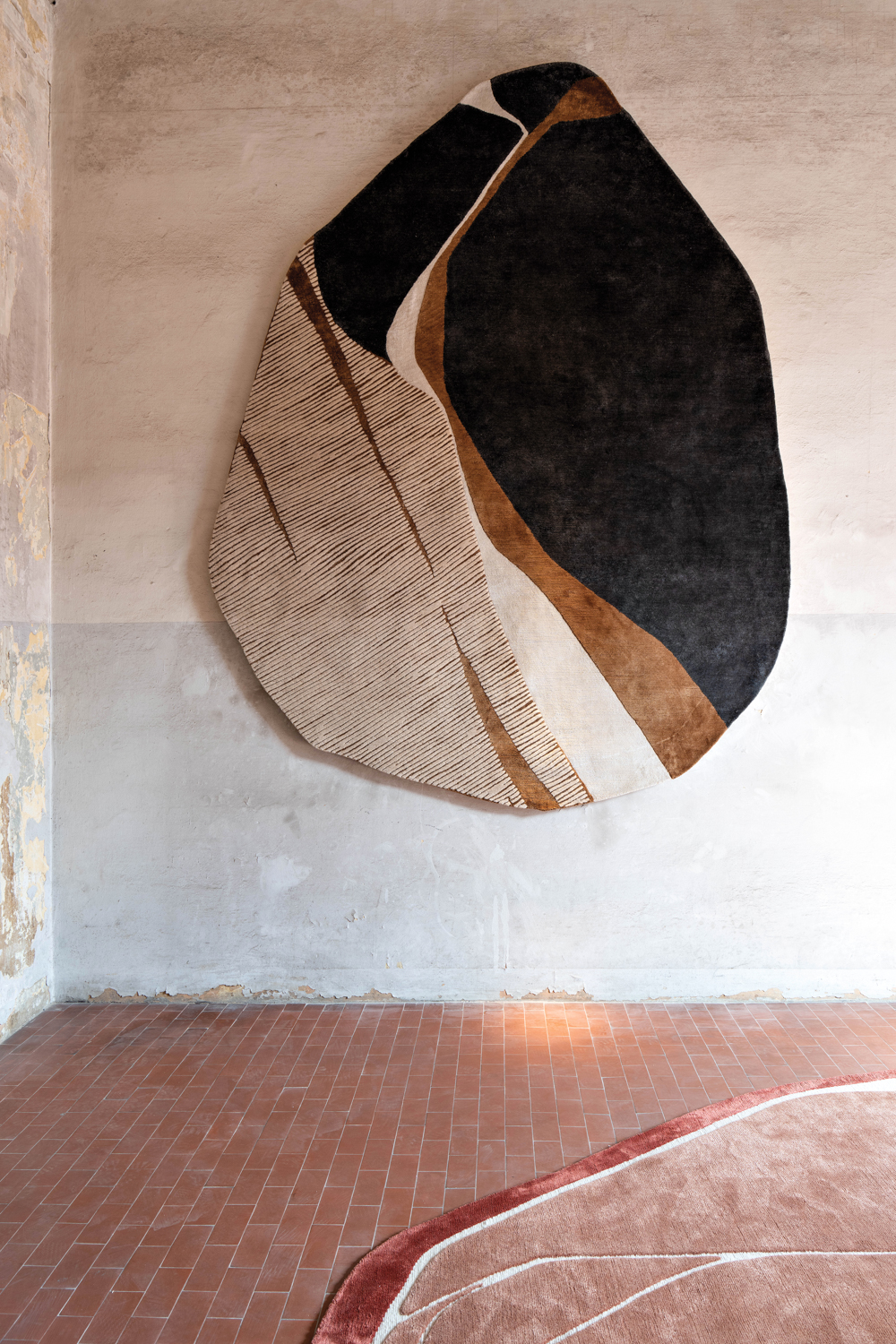 Black-, tan- and cream-colored circular-shaped rug hangs on blank wall above brick-lined floor