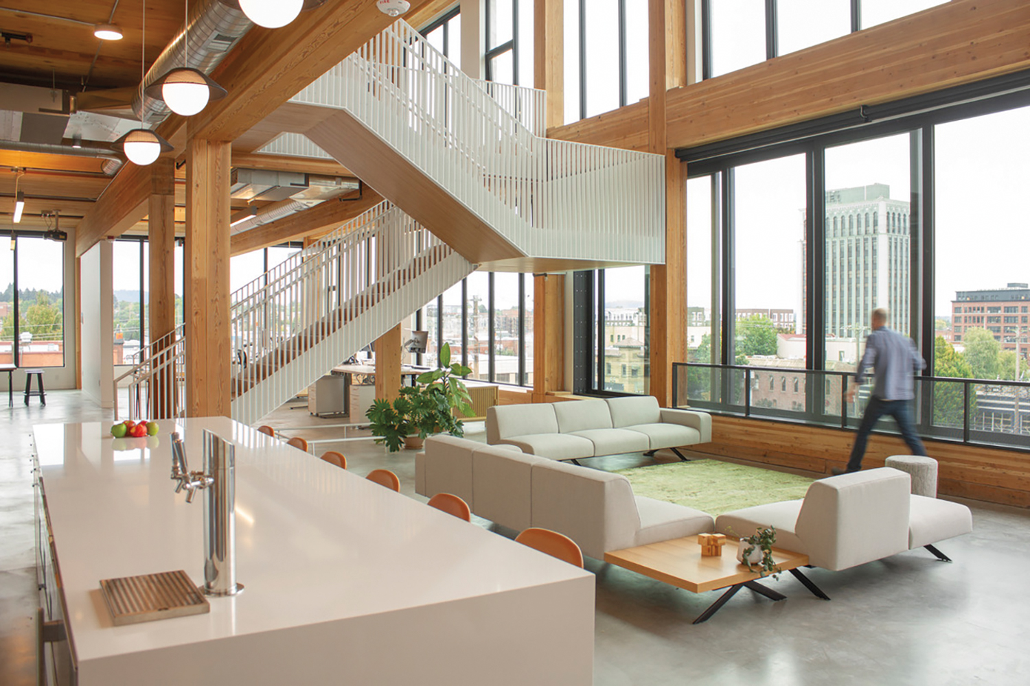 Double-height office space made of wood with white floating staircase and white sofas