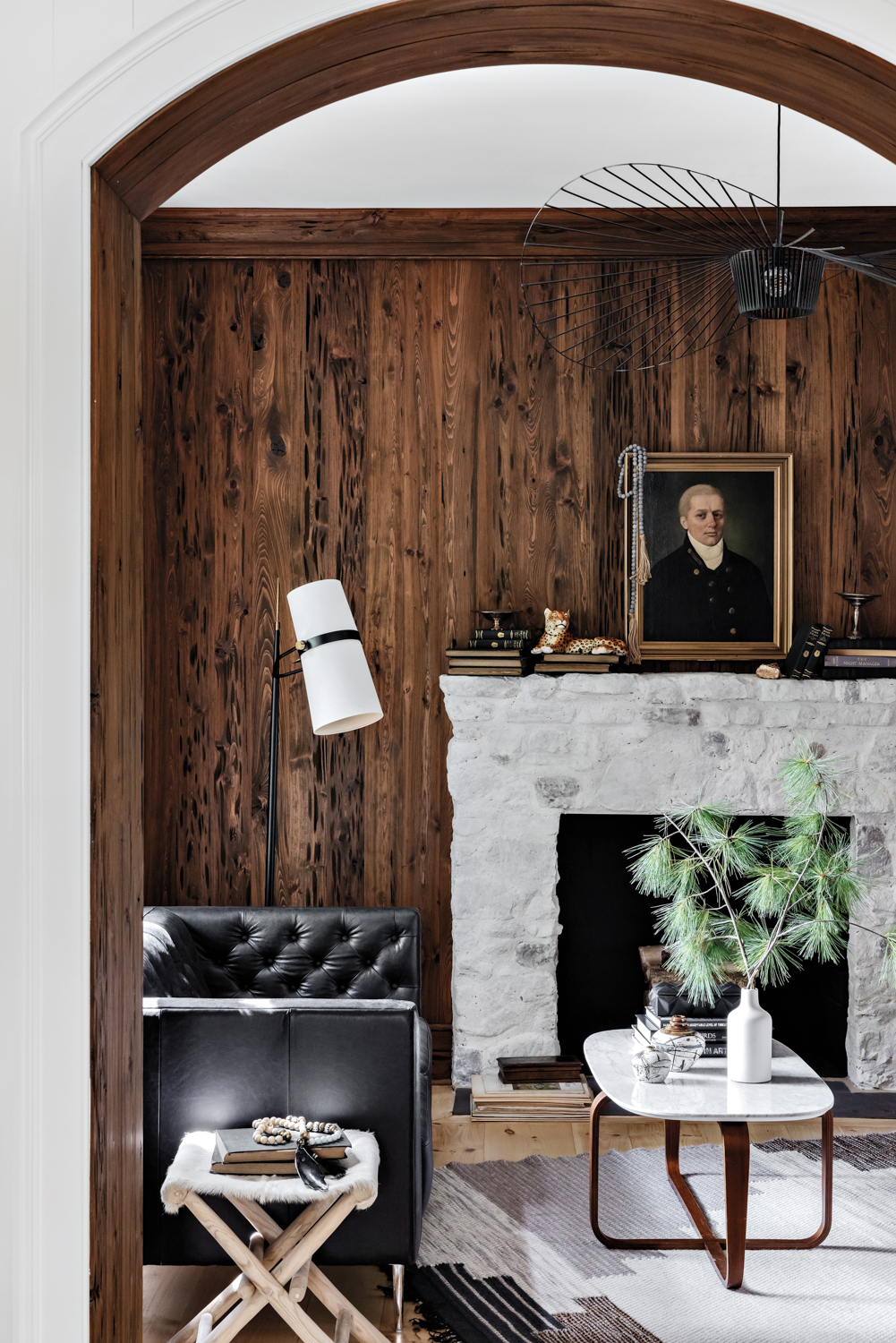 Dark wood wall paneling contrasts with white-washed stone fireplace and accented by a black-leather sofa