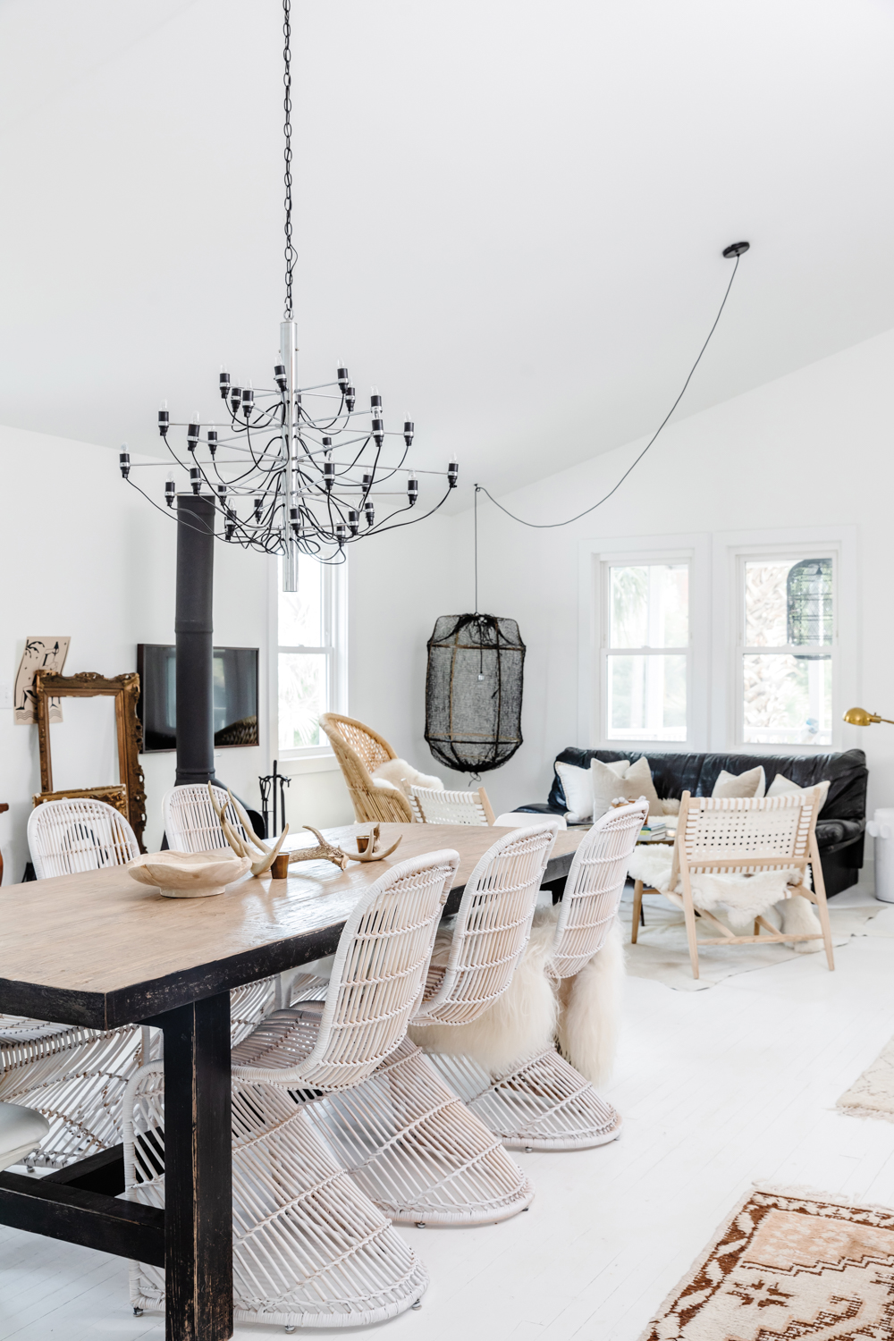 All-white dining room with a black chandelier above rectangular table with white wicker chairs.