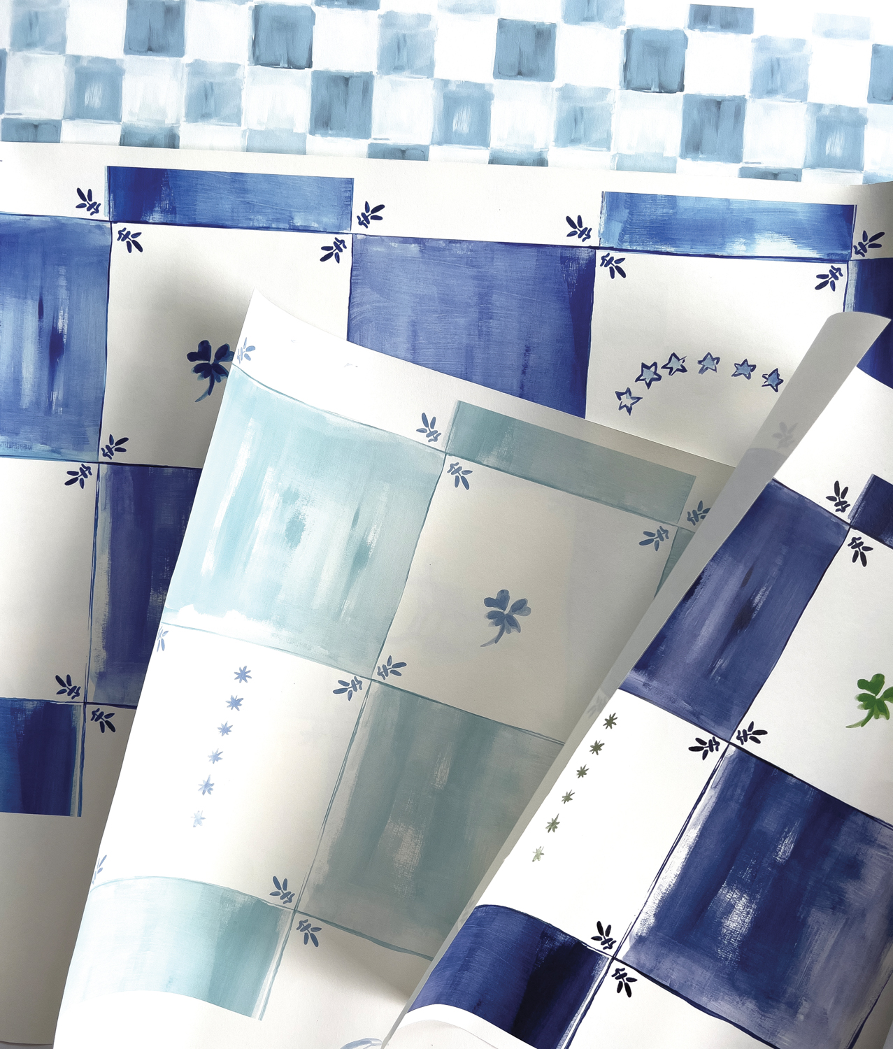 Wallcovering samples of blue-and-white checkered watercolor deigns featuring stars and clovers