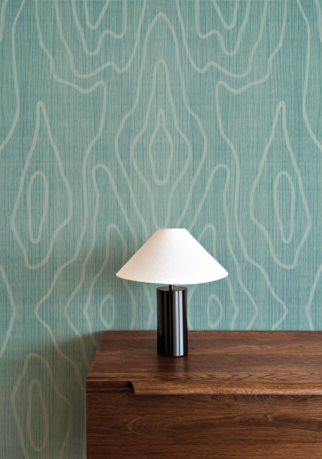 Teal-colored wallcovering behind dark wood side table and black table lamp with white shade