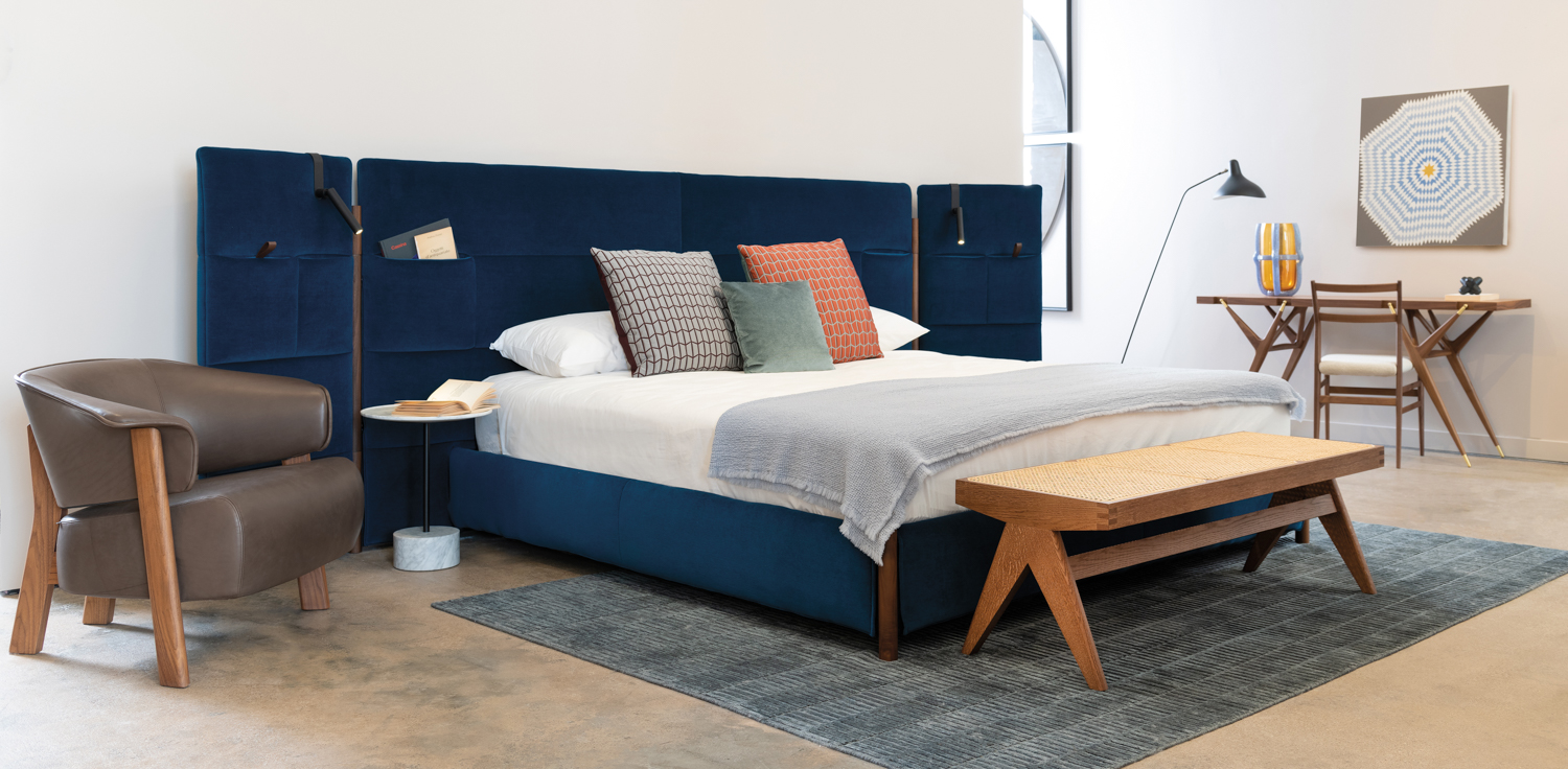 Scoot + Cooner showroom vignette grounded by a dark-blue-velvet bed with white linens
