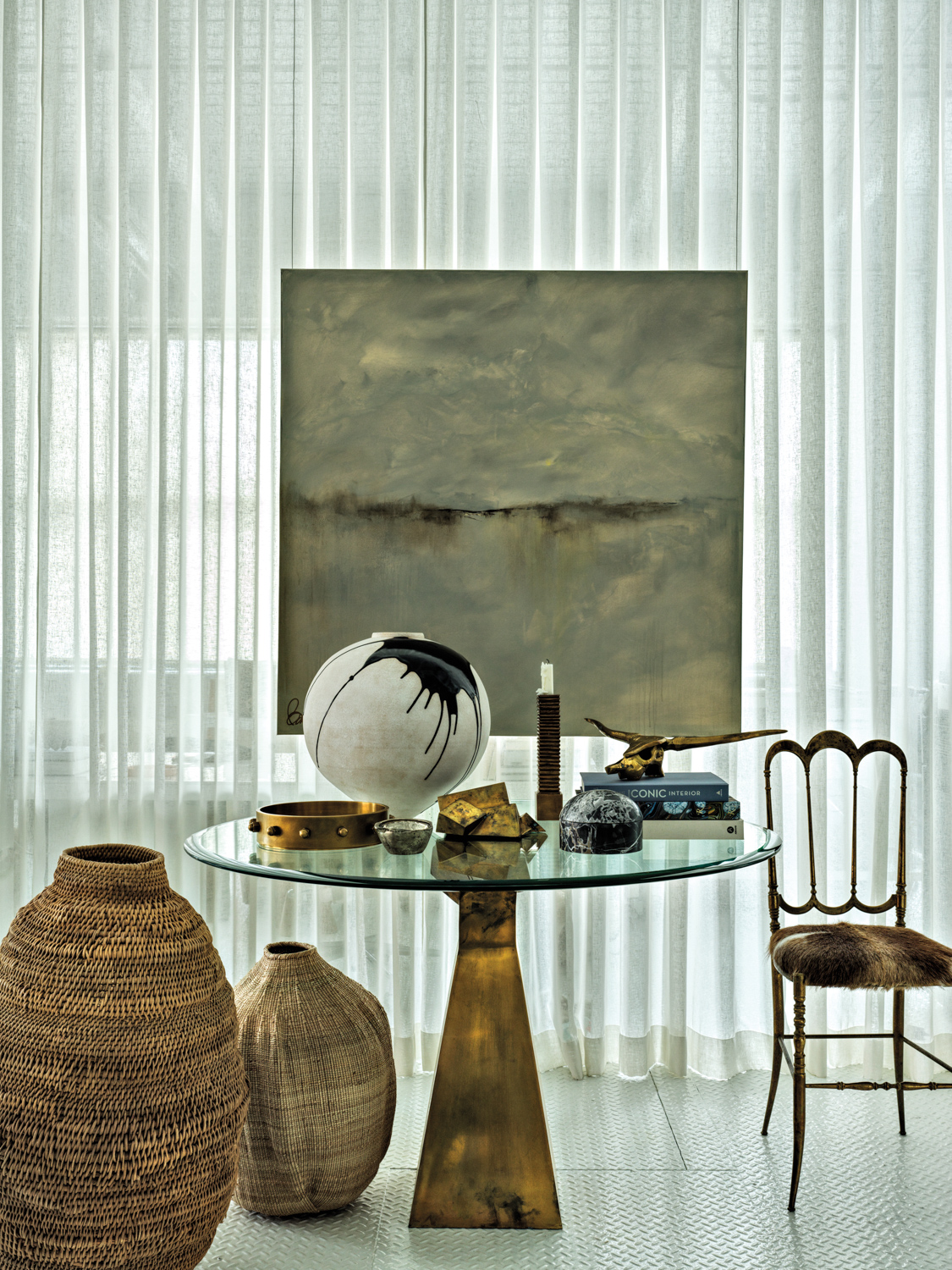 Moody abstract artwork overlooking a glass-topped table and textural oversize vases at Opame Collective