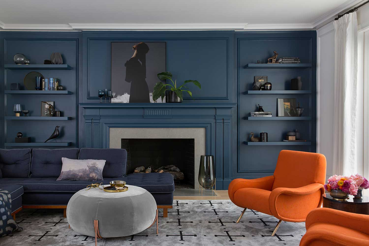 Top moody paint color Benjamin Moore's Gentleman's Grey cloaks a living room with fireplace and orange accent chairs