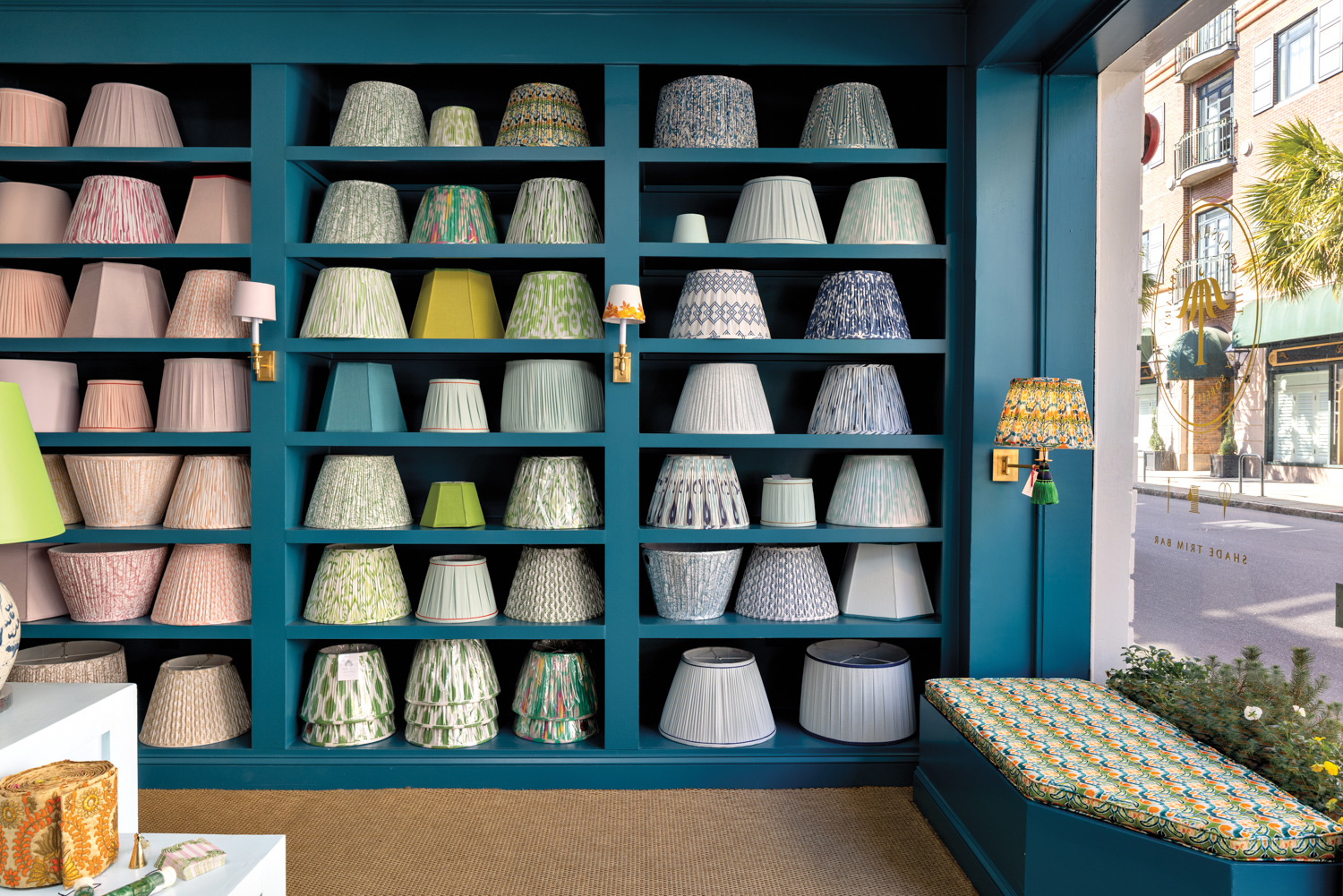 Wall of teal built-in shelves with color-coded pink, green and blue lampshades at the Lampshade Library