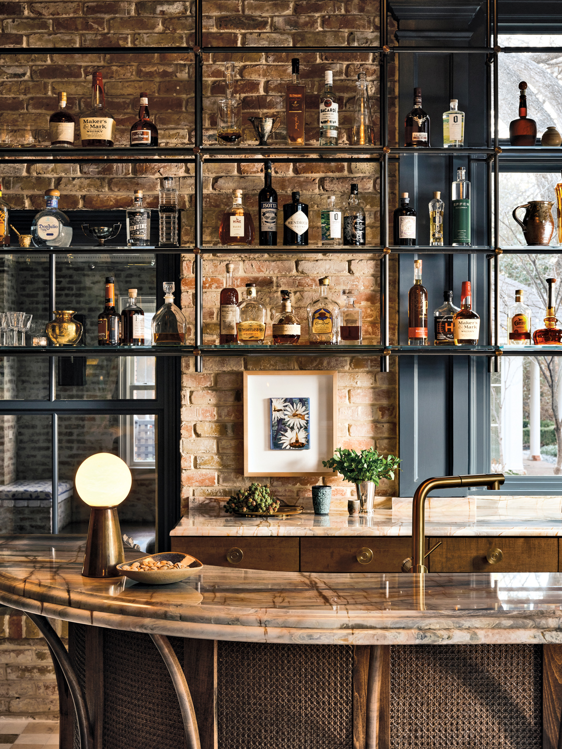 Rounded bar topped with natural stone, behind is exposed brick and exposed shelving displaying spirits.