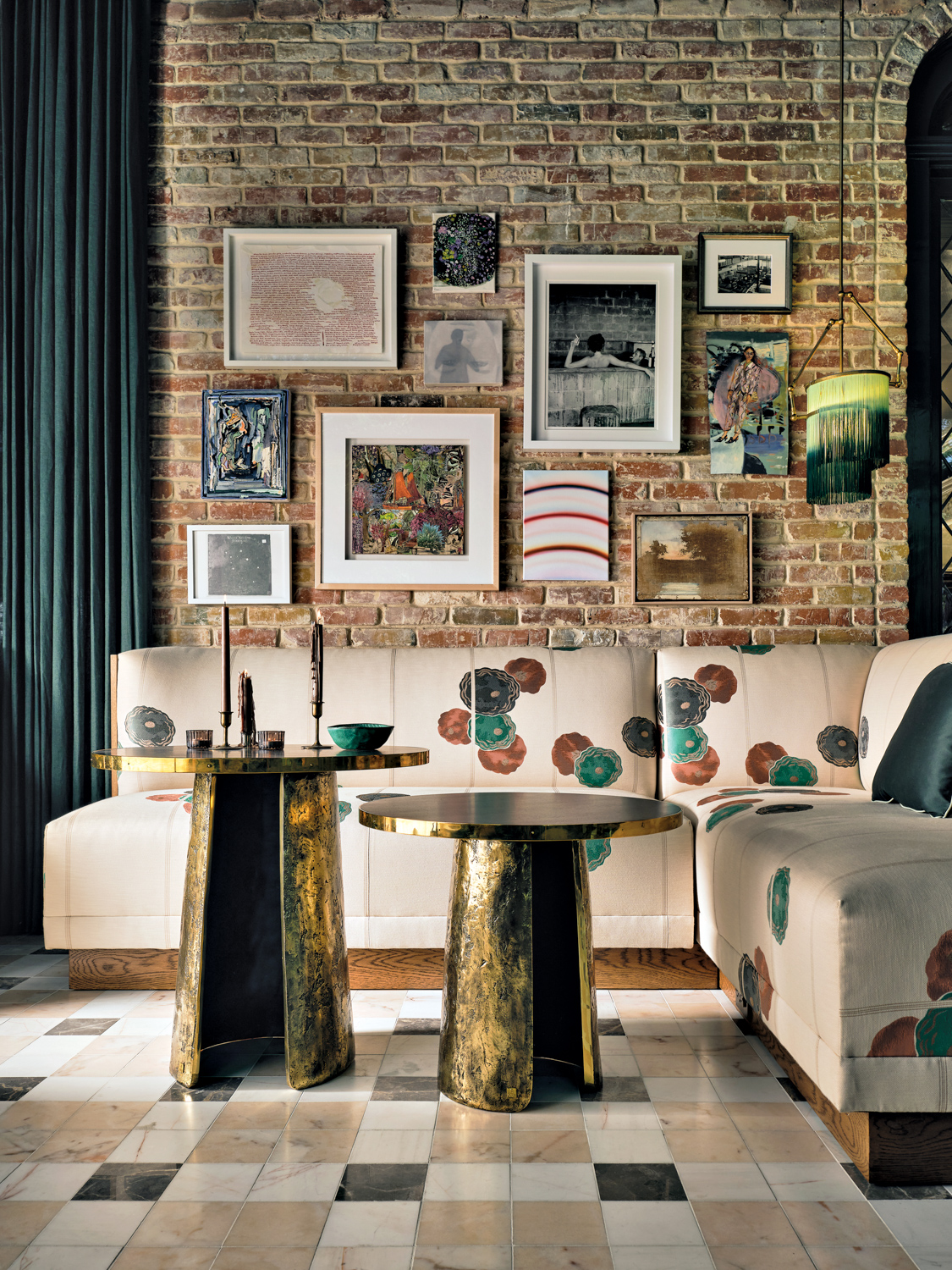 Gallery wall of artwork on exposed brick wall backs sectional banquette and set of 2 brass cocktail tables.